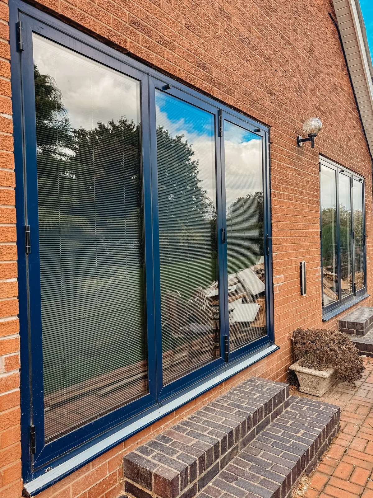 Garden-facing aluminium glazing set into red brickwork, with blinds visible behind the glass