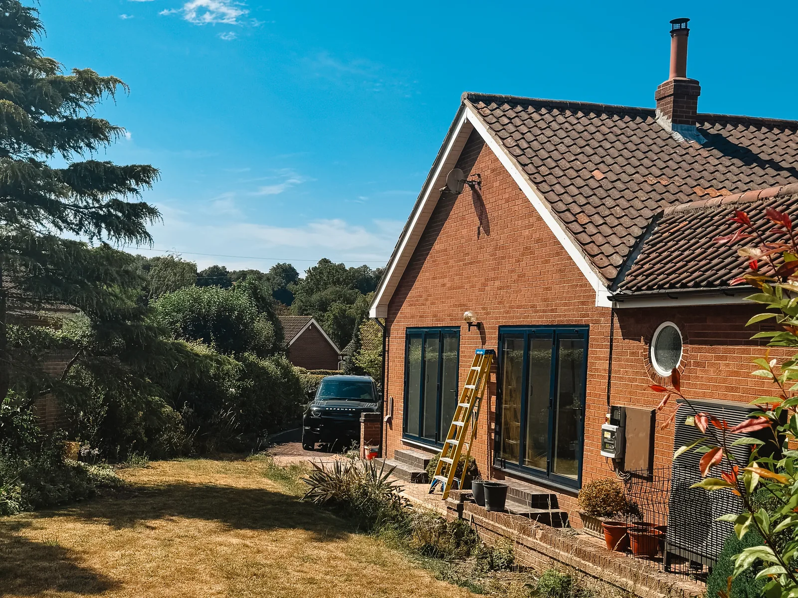 Dark aluminium windows overlooking the garden of a red-brick home during replacement work